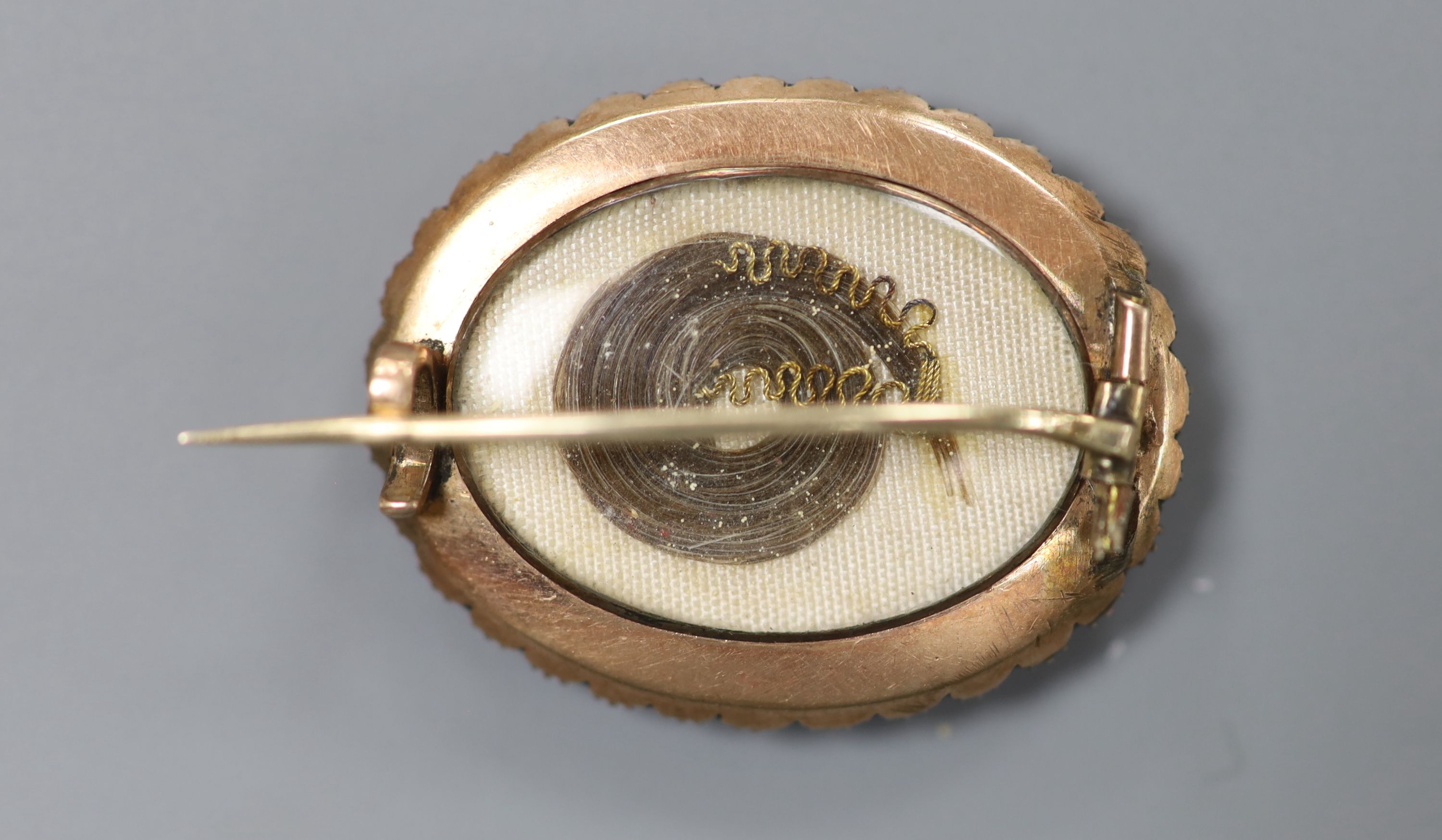 A Victorian yellow metal and split pearl set oval locket, with lock of plaited hair below a glazed panel, 27mm, gross 6.6 grams.